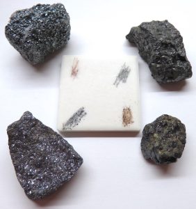 Four minerals around a white streak plate. Each mineral has been scratched on the plate and a colored powder left behind.