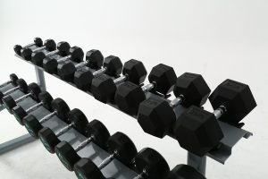 Two rows of black dumbbells on a grey rack against a white background