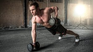 A ban with no shirtband black shorts is in a plank position while doing a row with barbells (also called a renegade row)